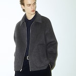Placeholder for: Person wearing a dark gray zip-up jacket over a navy shirt, looking to the side against a plain background.
