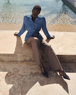 Placeholder for: Person sitting on a stone ledge by a pool, wearing a blue blouse and brown trousers, with chic black shoes.