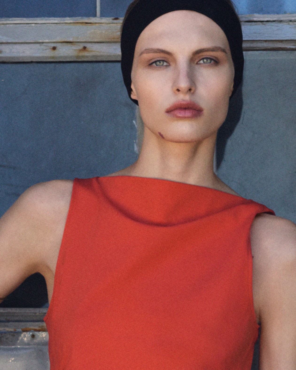 Person wearing a black headband and red sleeveless top, standing in front of a window with a neutral expression.