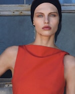 Placeholder for: Person wearing a black headband and red sleeveless top, standing in front of a window with a neutral expression.