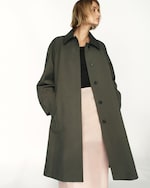 Placeholder for: A person wearing an oversized dark gray coat over a black top and a light pink skirt, standing against a plain background.