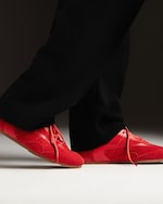 Placeholder for: Person wearing bright red sneakers and black pants, standing on a light surface with a dark background.