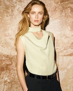 Placeholder for: A woman with long hair wearing a sleeveless beige top and black pants stands against a marble-patterned background.