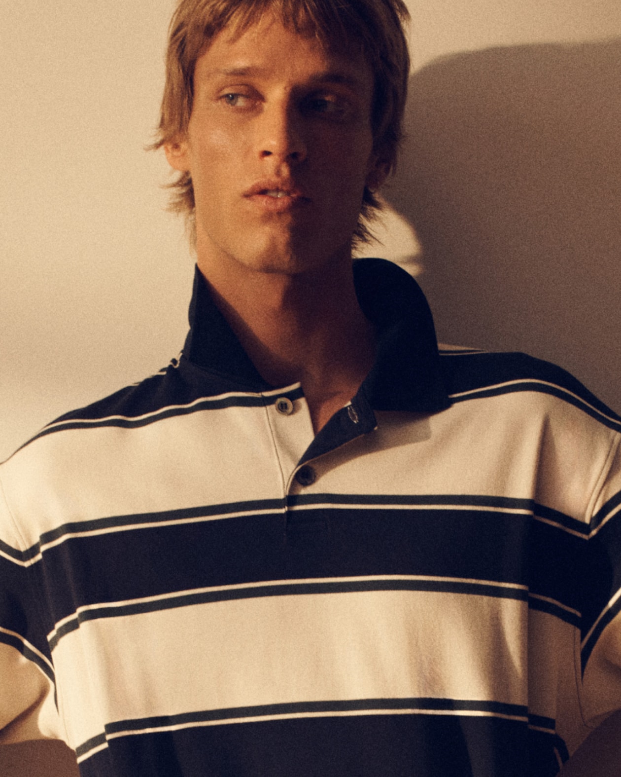 Person in a striped polo shirt looks to the side, lit by soft, warm lighting.