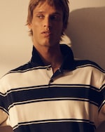 Placeholder for: Person in a striped polo shirt looks to the side, lit by soft, warm lighting.