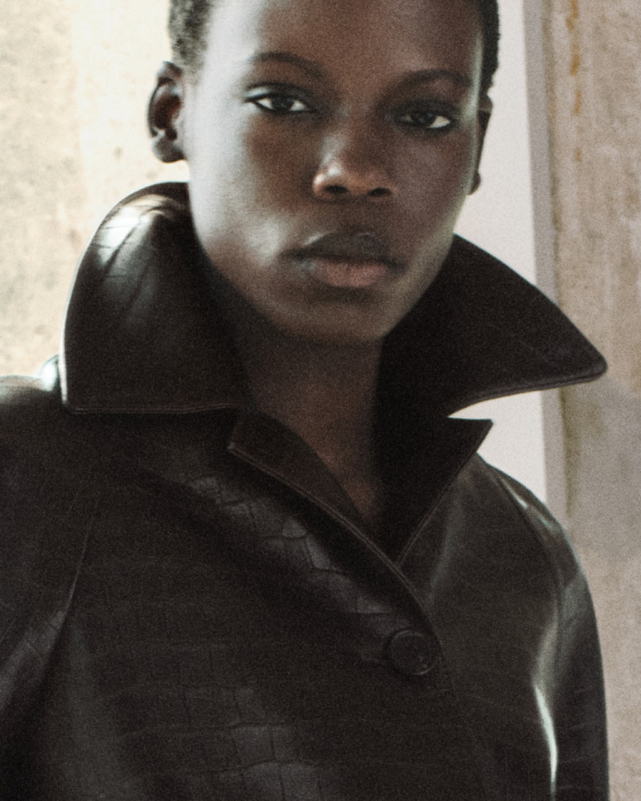 Close-up of a person in a dark textured leather coat with a high popped collar and neutral expression.