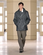 Placeholder for: Model wearing a dark, double-breasted coat with hands in pockets, paired with loose brown pants, walking in a minimalist setting.