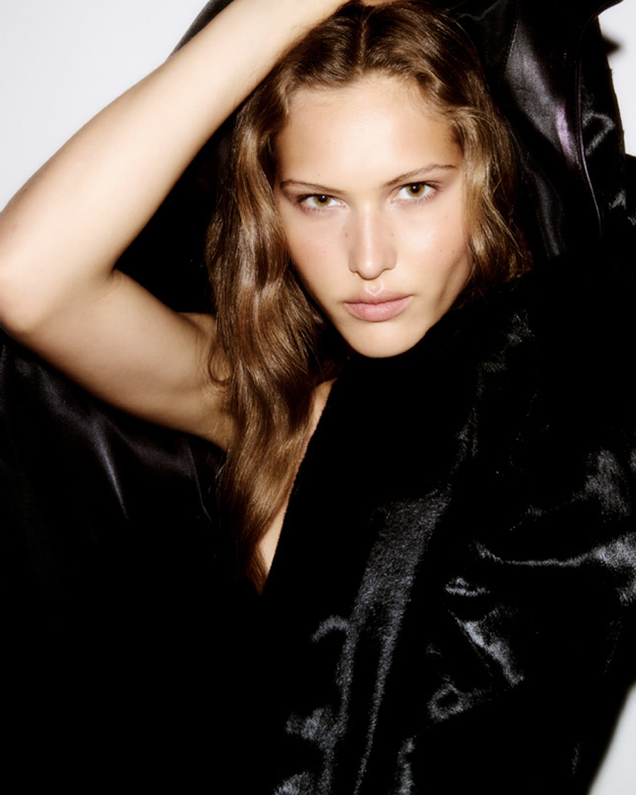 Person with long hair wrapped in a black satin-like fabric, gazing directly at the camera with a neutral expression.