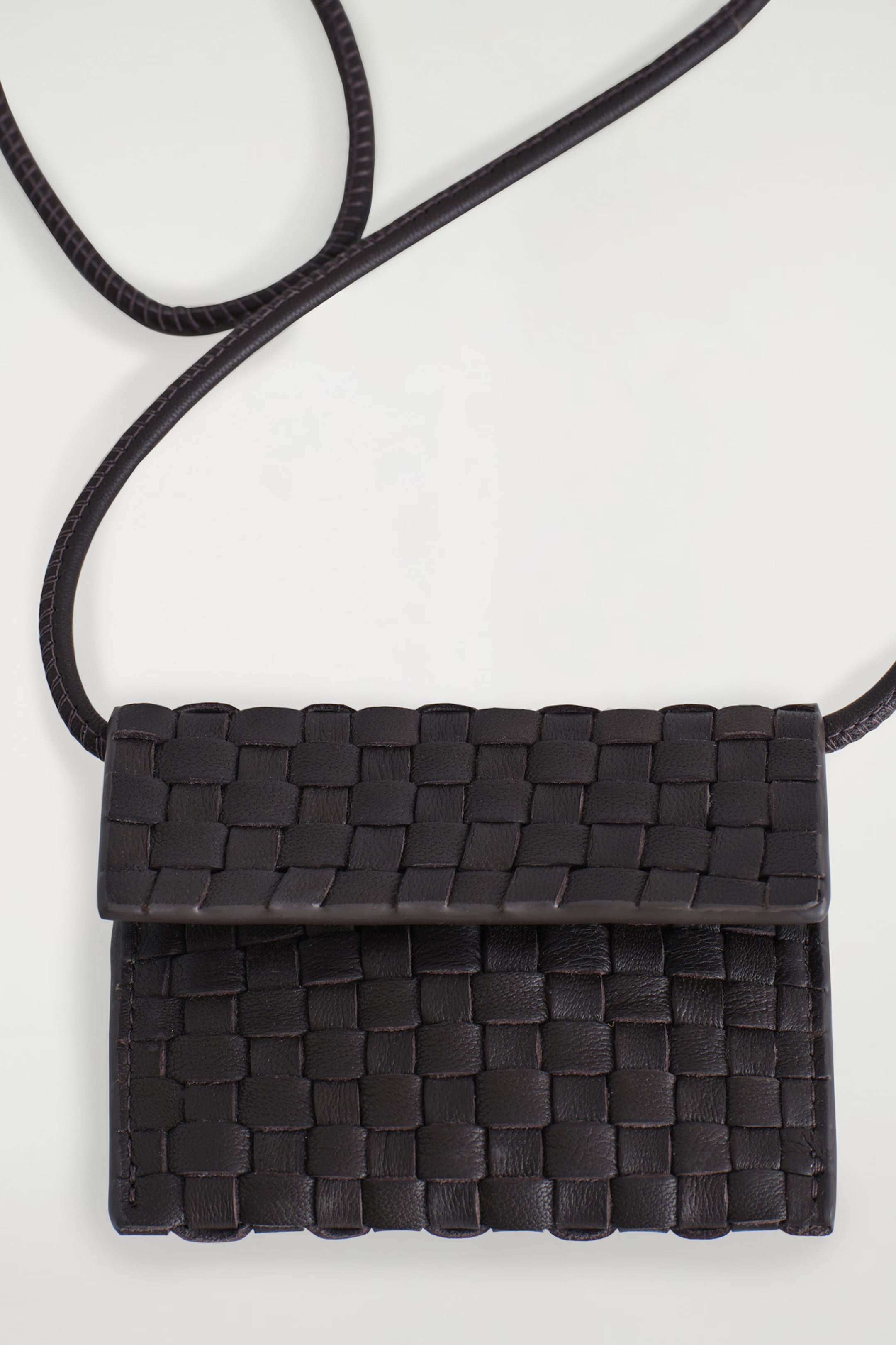 A small, black woven leather crossbody bag with a long strap, displayed against a white background.