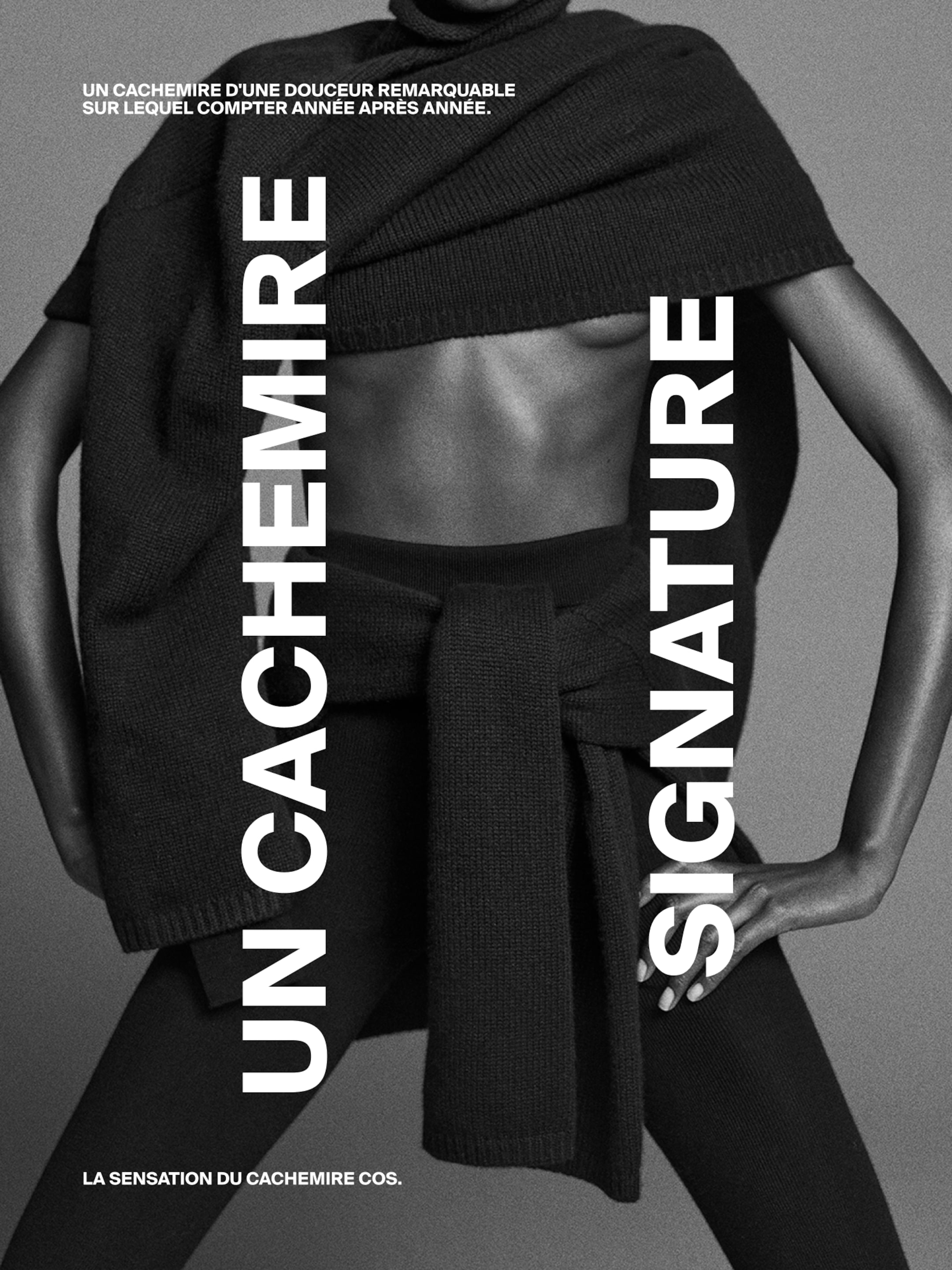 A person wearing an elegantly draped cashmere garment, posed against a gray background, with text in French promoting signature cashmere.