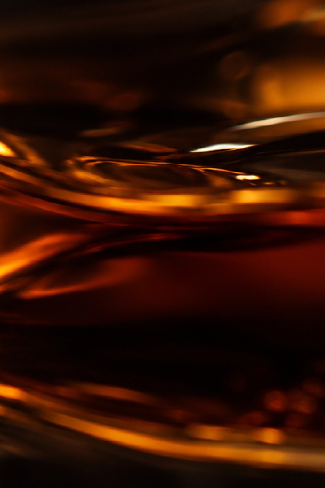 Abstract close-up of swirling golden liquid with reflections and highlights, creating a warm and dynamic visual effect.