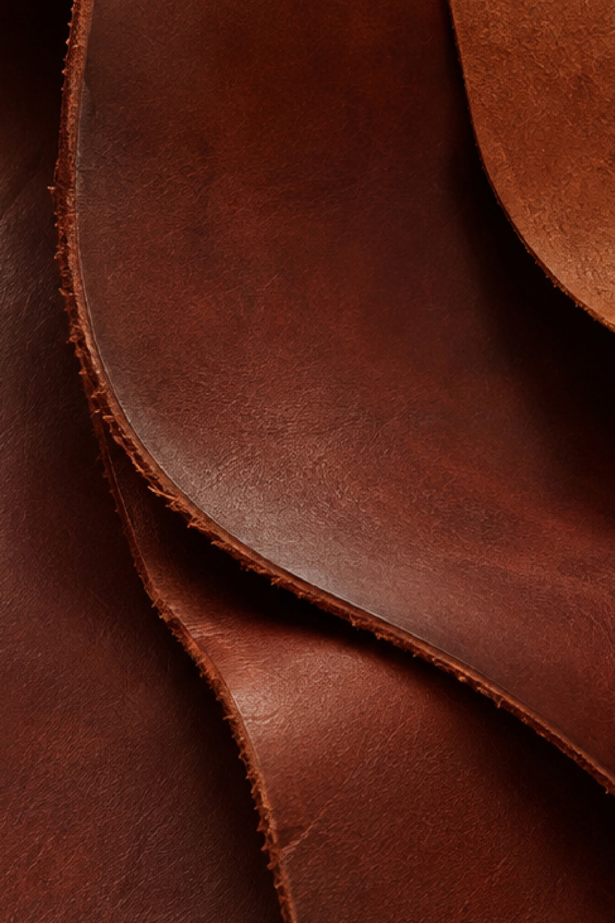 Close-up of overlapping sheets of brown leather with visible texture and rough edges.