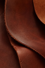Placeholder for: Close-up of overlapping sheets of brown leather with visible texture and rough edges.
