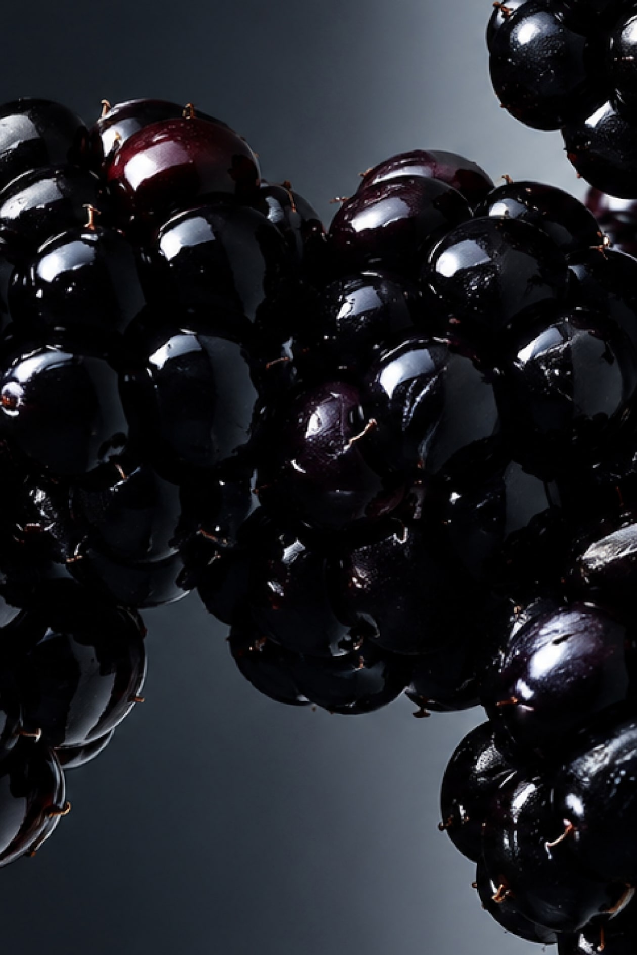 Close-up of shiny, dark blackberries with a glossy finish, against a dark background.