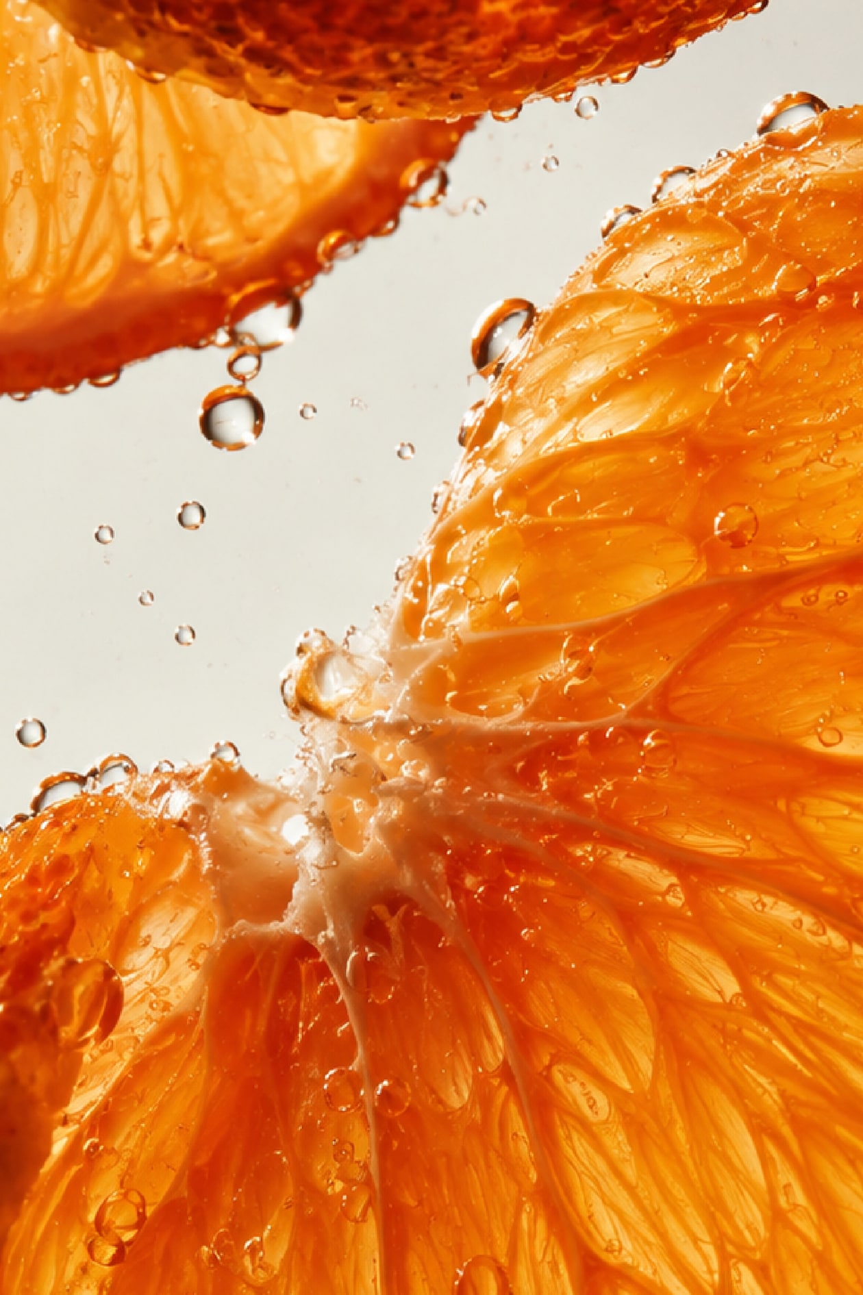 Close-up of juicy orange slices with water droplets, showing detailed texture and vibrant orange color against a light background.