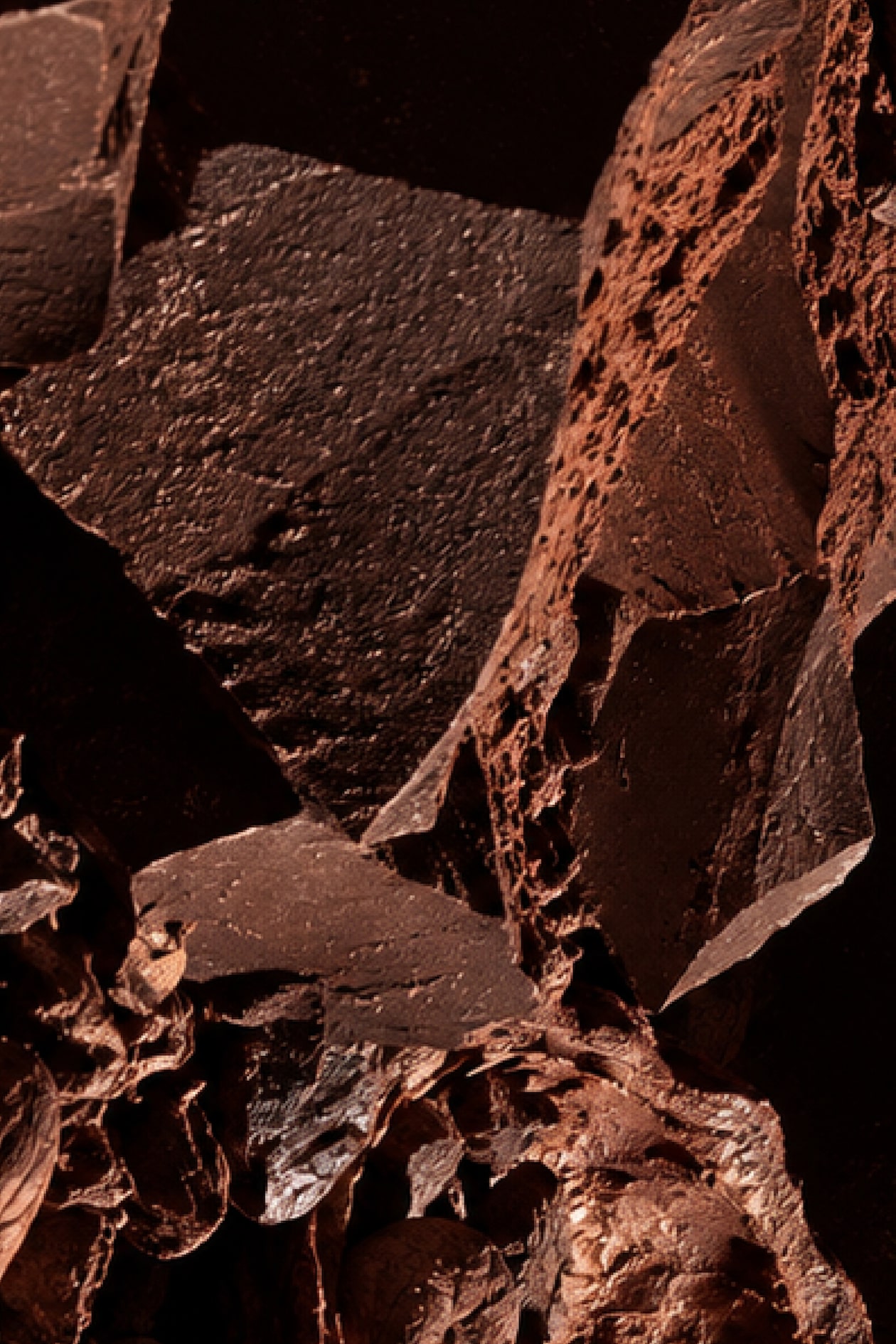 Close-up of dark, textured chocolate pieces with jagged edges and cocoa dust, creating a rugged, abstract pattern.