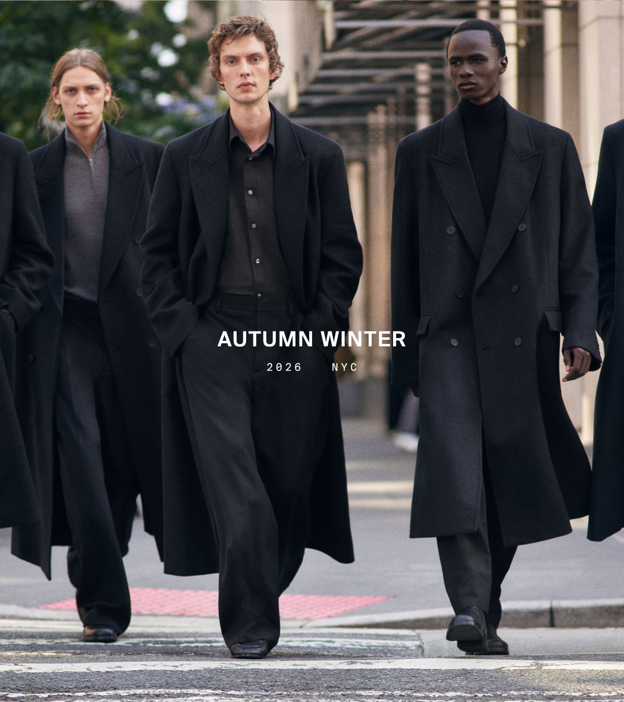 Models wearing long black coats walk confidently on a city street. Text reads "Autumn Winter 2026 NYC."