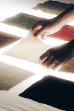 Placeholder for: Hands arranging felt swatches of various colors under bright lighting.