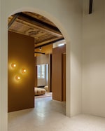 Placeholder for: Elegant interior with arched doorway, warm brown walls, circular wall lights, and a view of a cozy seating area with natural light.