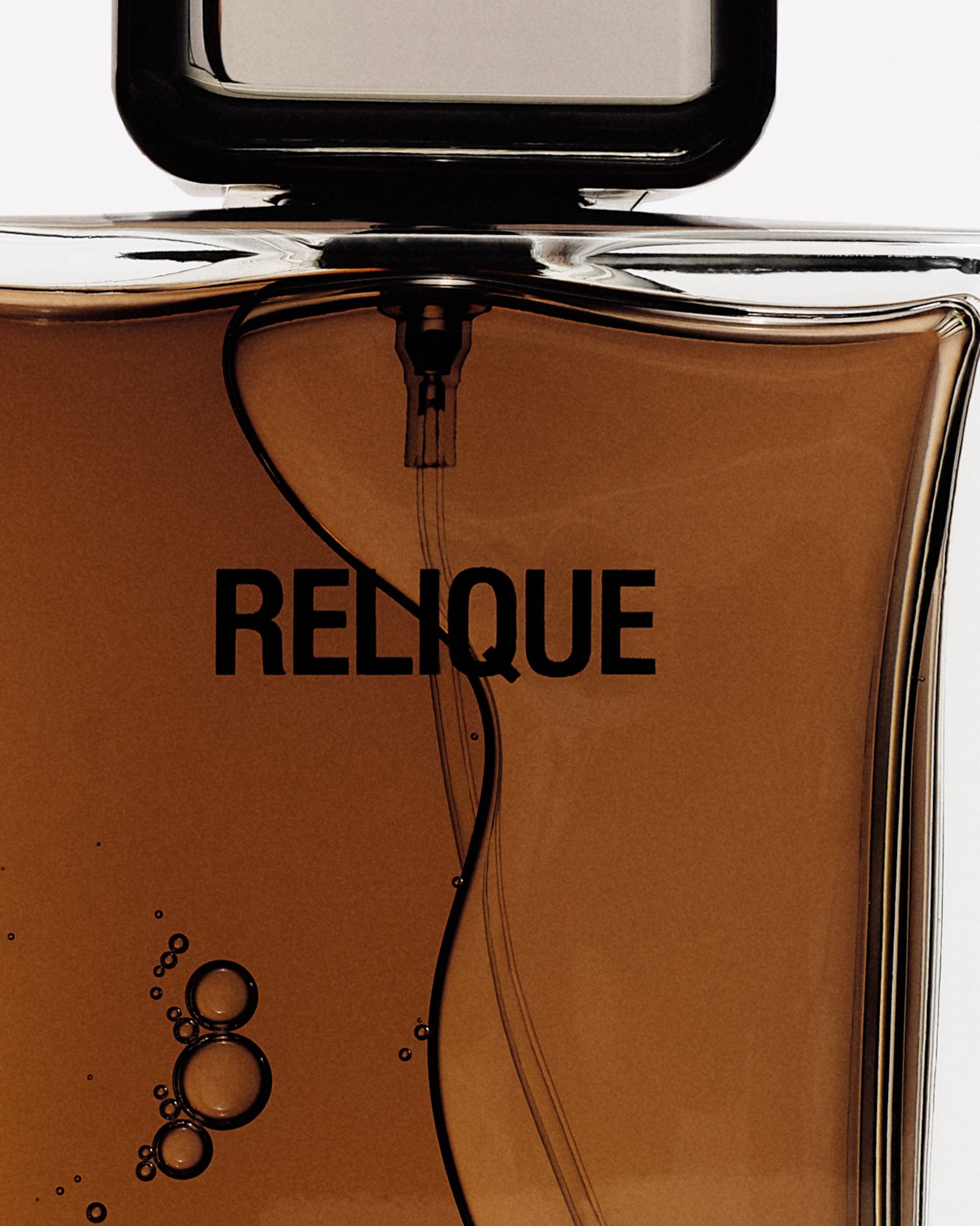 Close-up of a brown liquid-filled perfume bottle with the word "RELIQUE" on it, a pipette inside, and air bubbles visible.