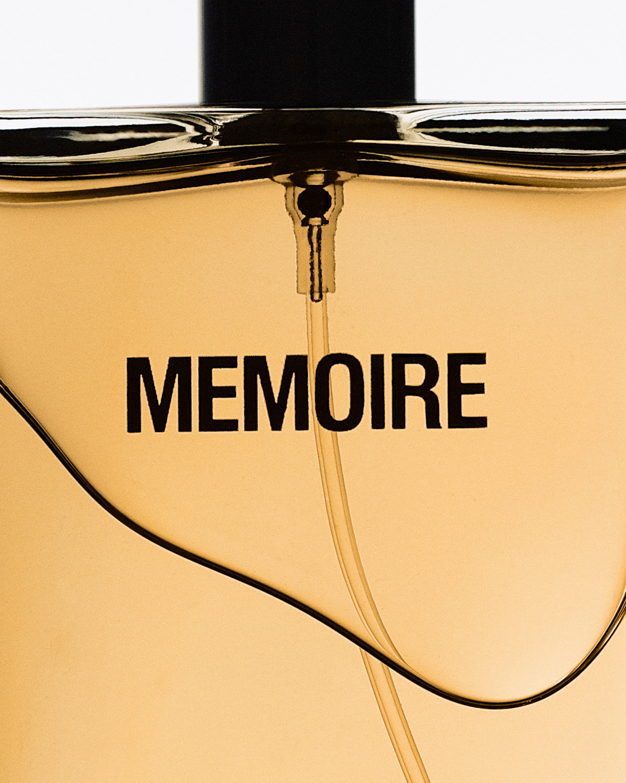 Close-up of a perfume bottle with "MEMOIRE" written on it, featuring a golden hue and a stylish curved design.