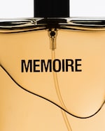 Placeholder for: Close-up of a perfume bottle with "MEMOIRE" written on it, featuring a golden hue and a stylish curved design.