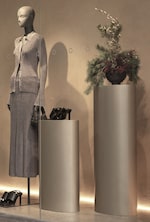 Placeholder for: 2 grey podiums, one with flowers on it and one with shoes on it next to a mannequin