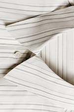 Placeholder for: Close-up of a neatly folded, beige pinstripe shirt with visible collar and buttons.
