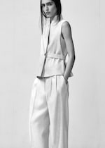 Placeholder for: A person wearing a sleeveless vest and wide-legged pants poses against a plain backdrop, exuding a minimalist fashion style.