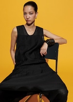 Placeholder for: A person in a black sleeveless outfit sits on a chair against a vibrant yellow background, wearing hoop earrings and layered bracelets.
