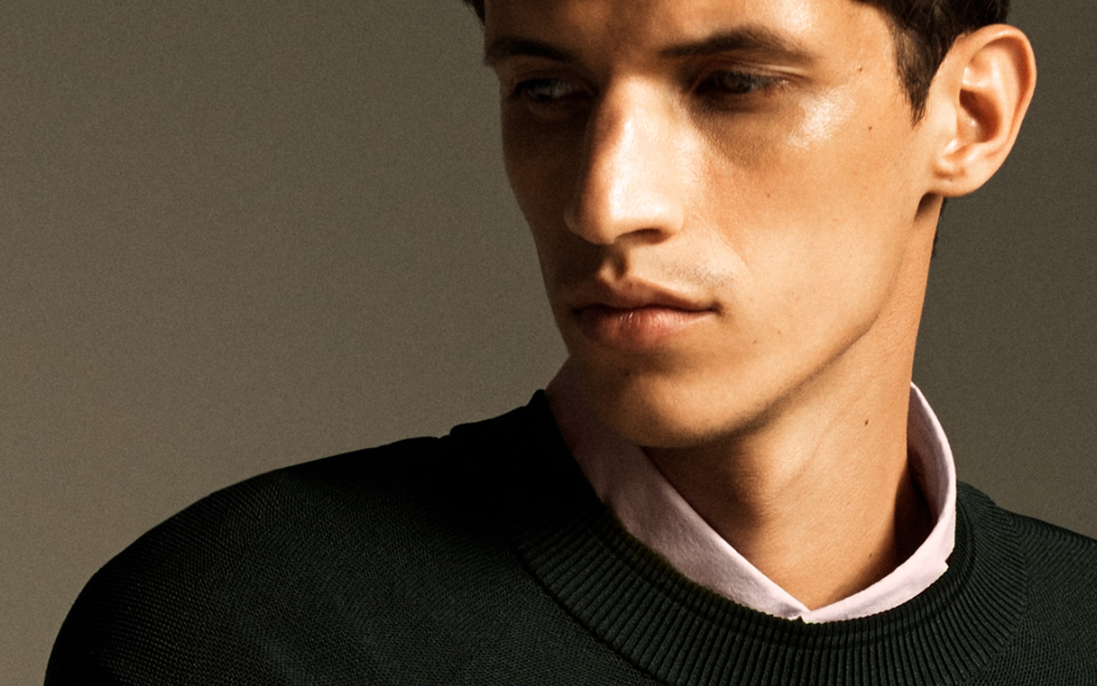 Man in a dark sweater and light shirt looking to the side against a neutral background.