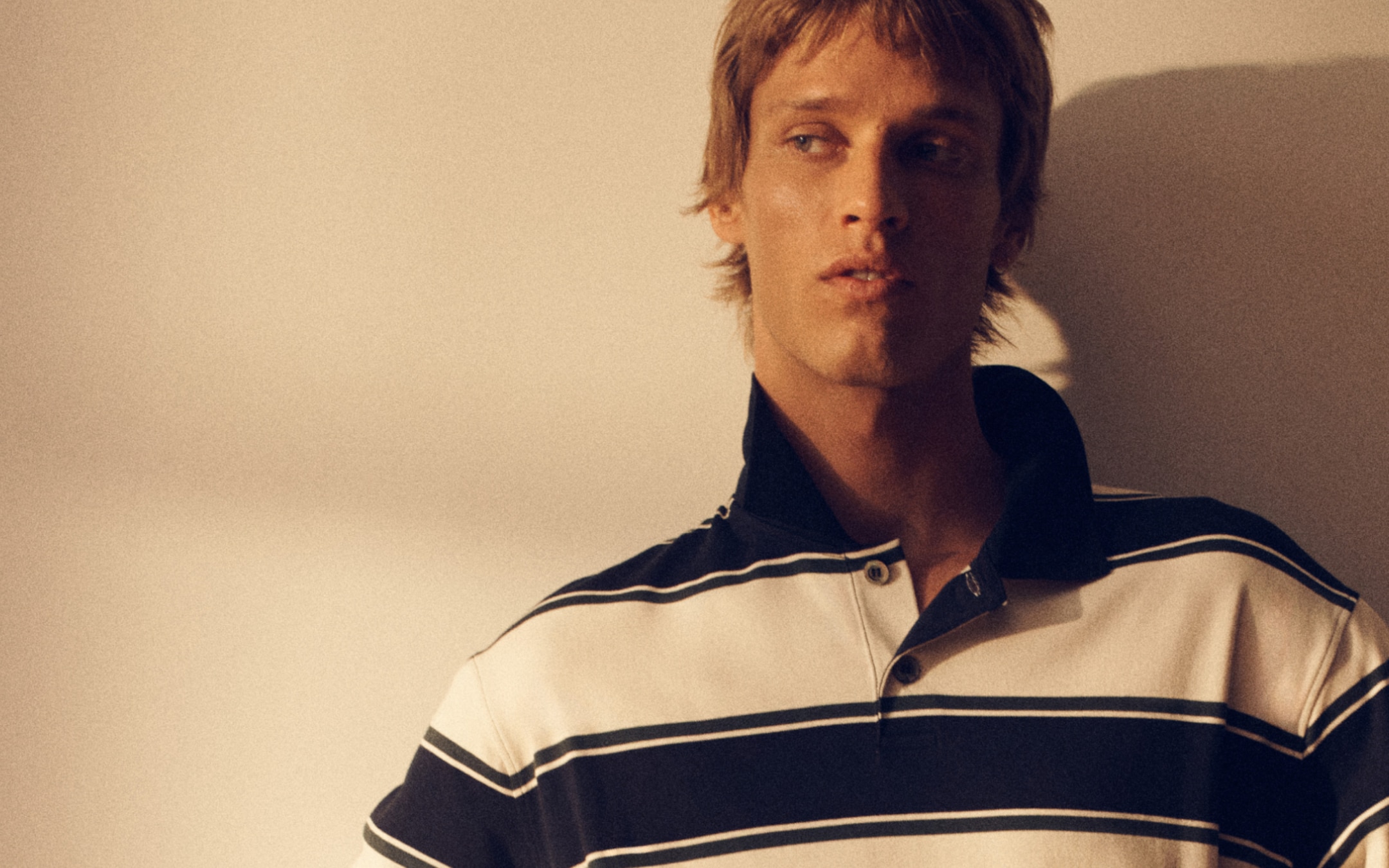 Person wearing a striped polo shirt, looking to the side, with a neutral expression, set against a neutral background.
