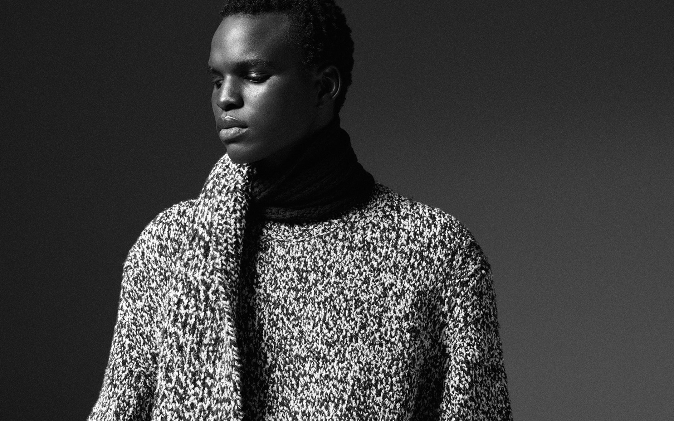 Black and white portrait of a person in a textured knit sweater, gazing thoughtfully to the side.