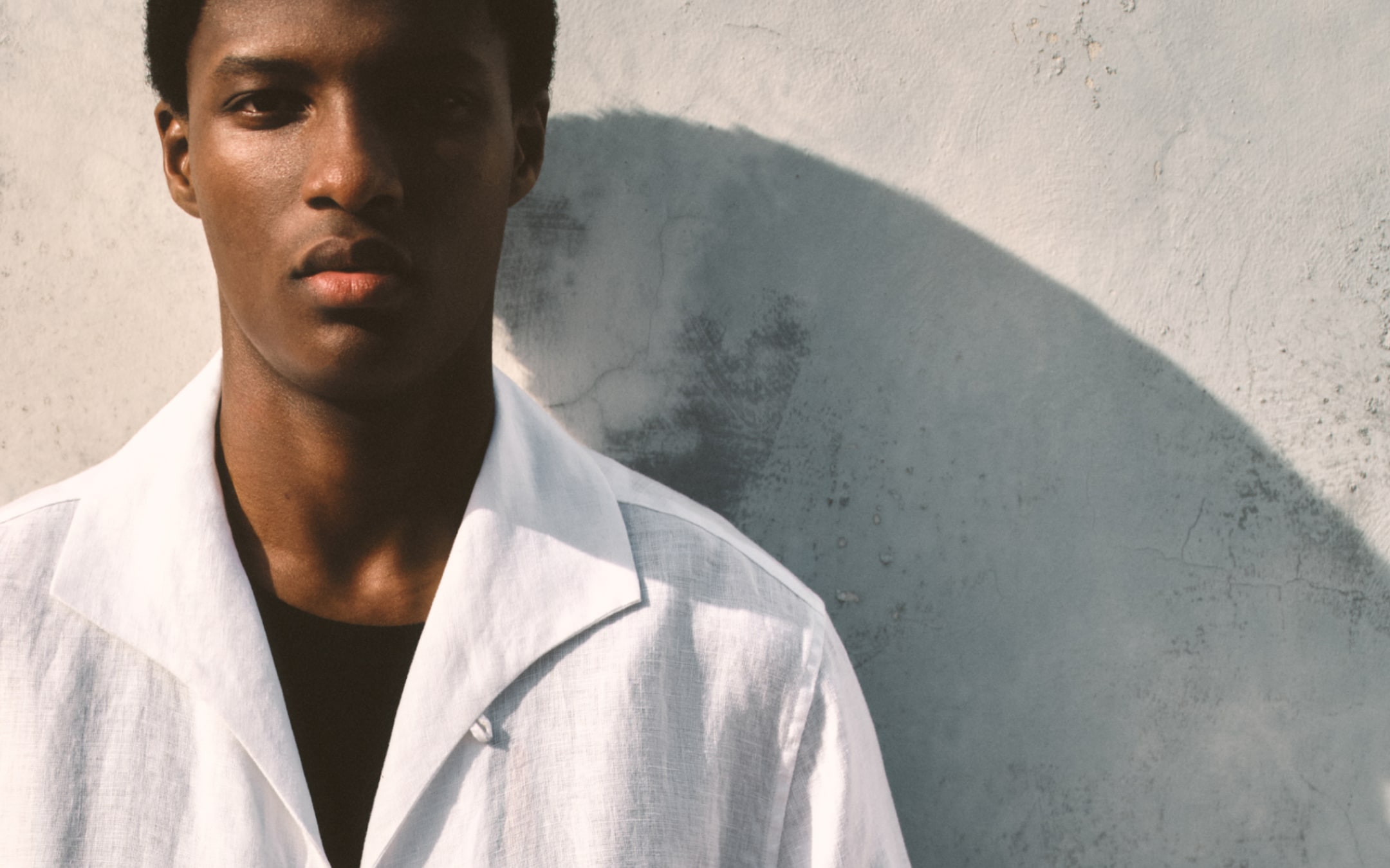 Model wearing a white linen shirt and leaning against the wall.
