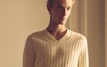 Placeholder for: Close-up portrait of a blond young man in a cream ribbed V-neck sweater, soft warm lighting and neutral background.