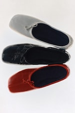 Placeholder for: Three pairs of leather slip-on shoes in white, black, and red, each with a small bow, arranged in a vertical stack on a white background.