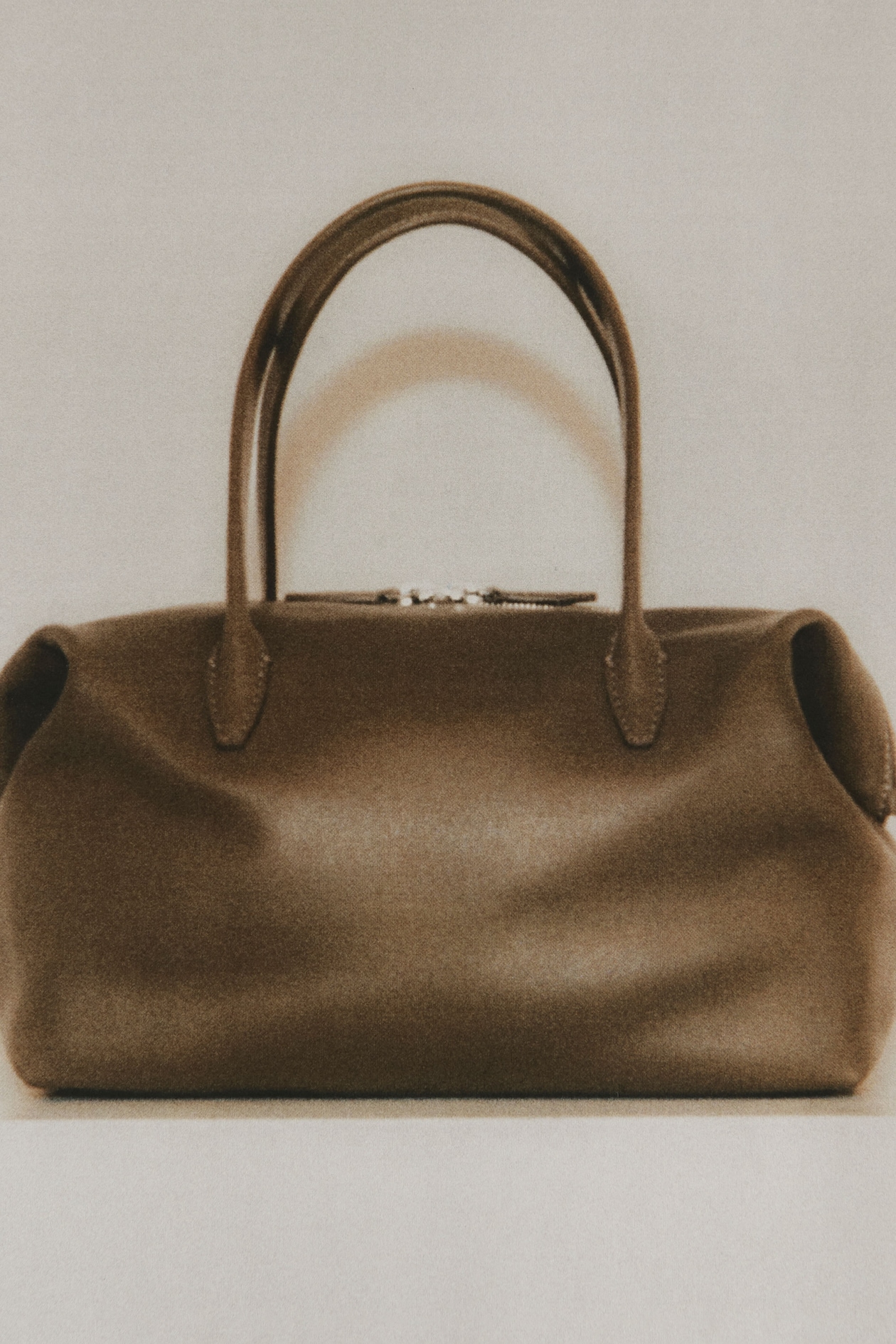 Brown leather handbag with rounded handles and a sleek, minimalist design, set against a neutral background.