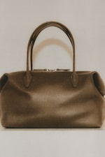 Placeholder for: Brown leather handbag with rounded handles and a sleek, minimalist design, set against a neutral background.