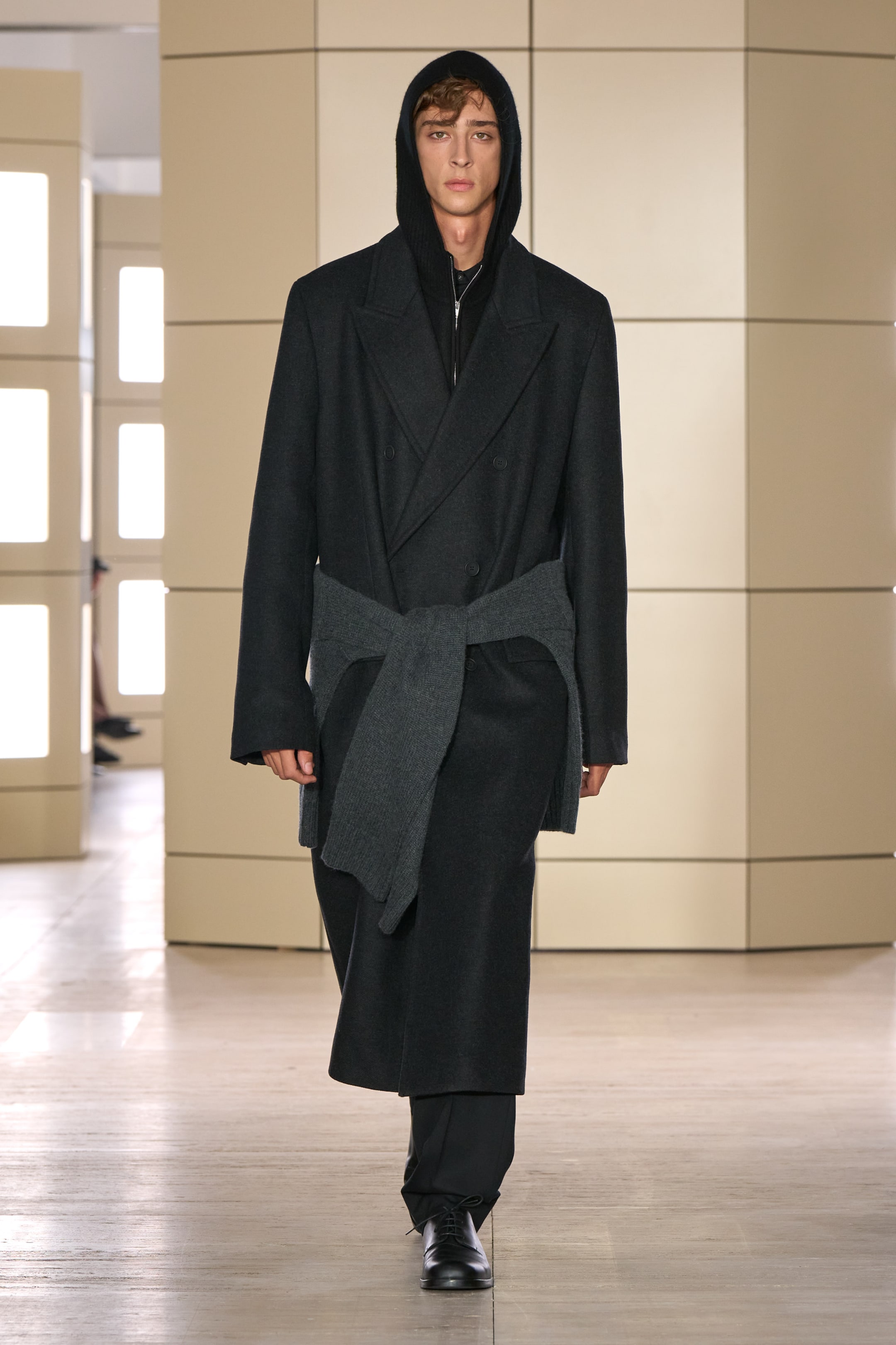 Person walking on a runway wearing a black wool coat