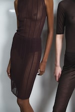 Placeholder for: Two models wearing sheer, dark-colored outfits. One outfit is a sleeveless dress; the other includes a short-sleeve shirt and pants.