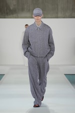 Placeholder for: Model in a gray oversized suit and cap walks down a bright runway with a minimalist background.