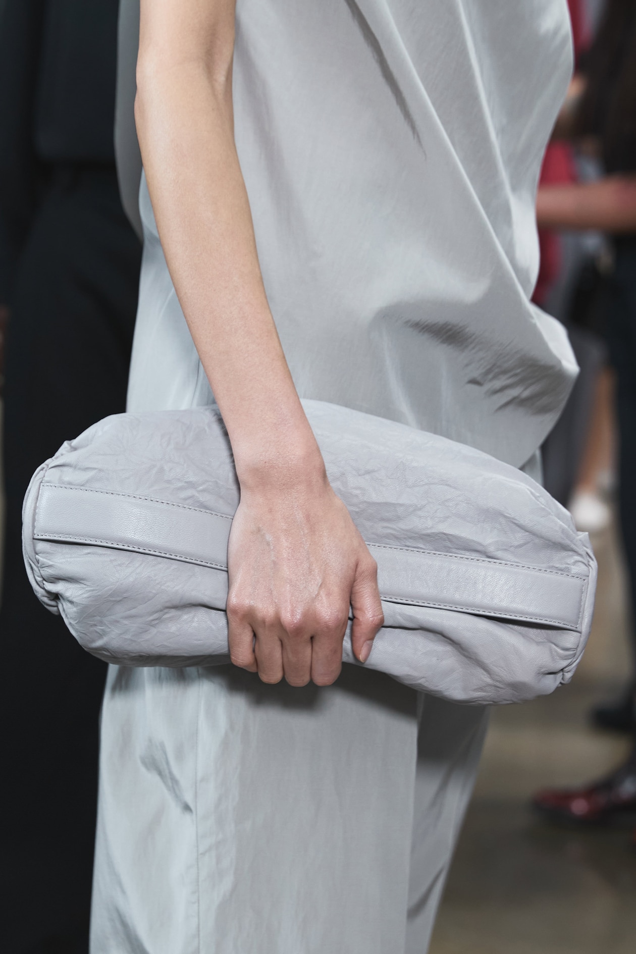 Person holding a large, light gray cylindrical clutch bag, wearing a matching gray outfit.