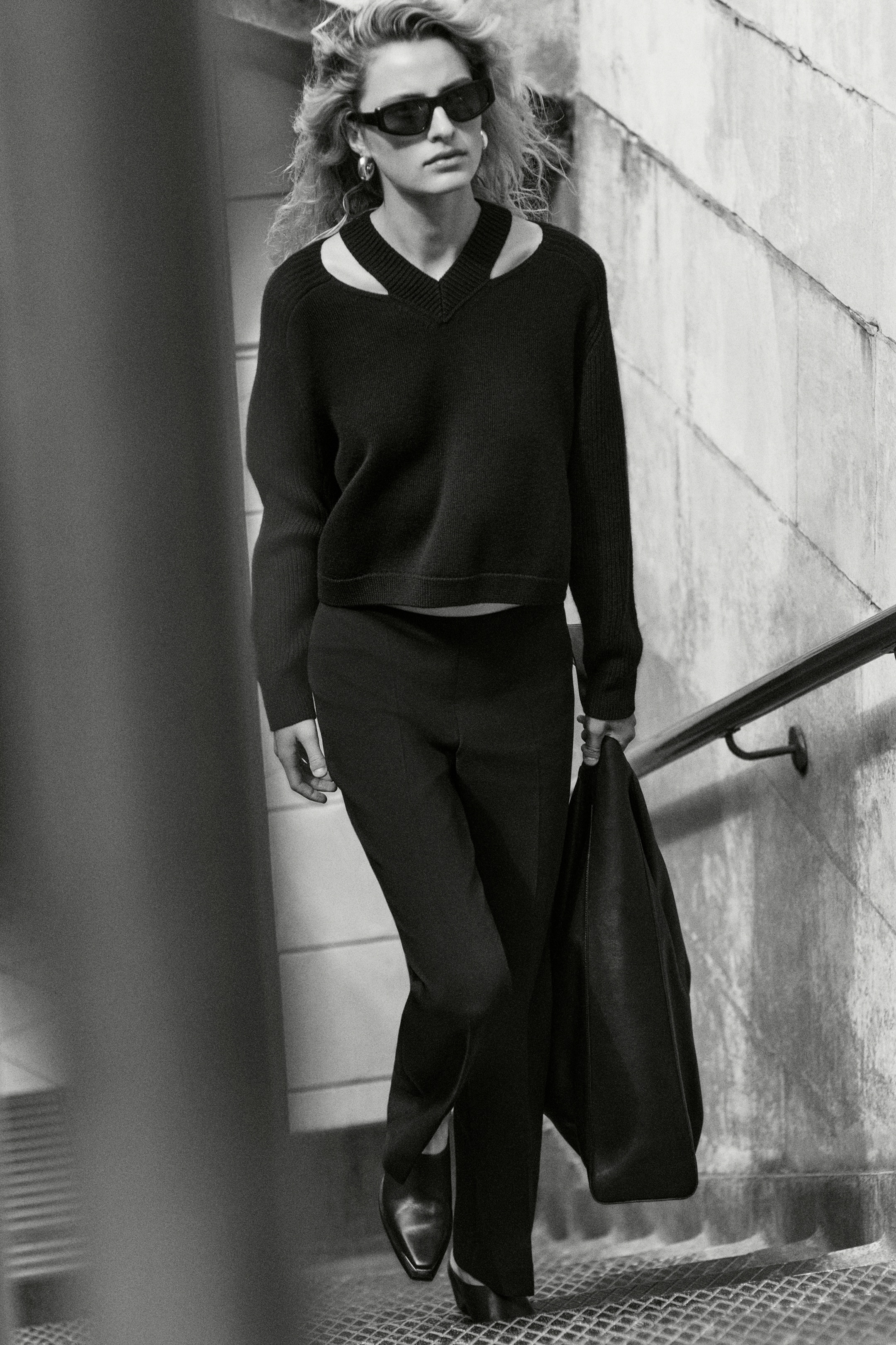 Person wearing black top, trousers, shoes and sunglasses going up stairs