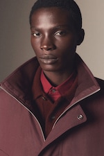 Placeholder for: Person wearing a burgundy jacket and shirt, looking directly at the camera against a neutral background.