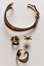 Placeholder for: Gold jewelry set featuring a twisted open bangle, hoop earrings, and knot stud on a neutral background.