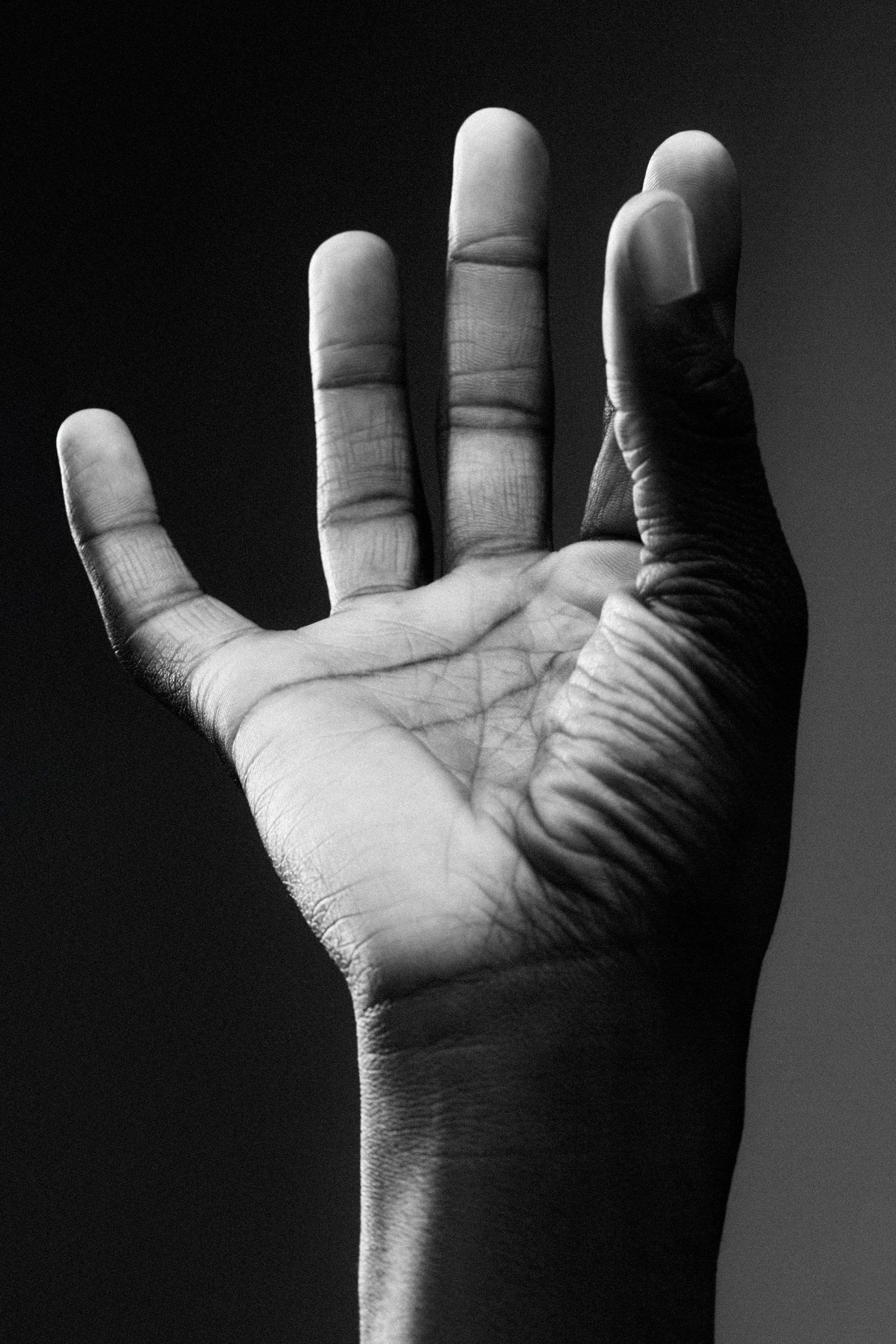 Close-up of an open hand with fingers spread, seen in black and white, against a dark background.