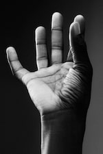 Placeholder for: Close-up of an open hand with fingers spread, seen in black and white, against a dark background.