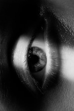Placeholder for: Close-up black and white image of an eye with detailed iris and glistening eyelashes, showing contrast between light and shadow.