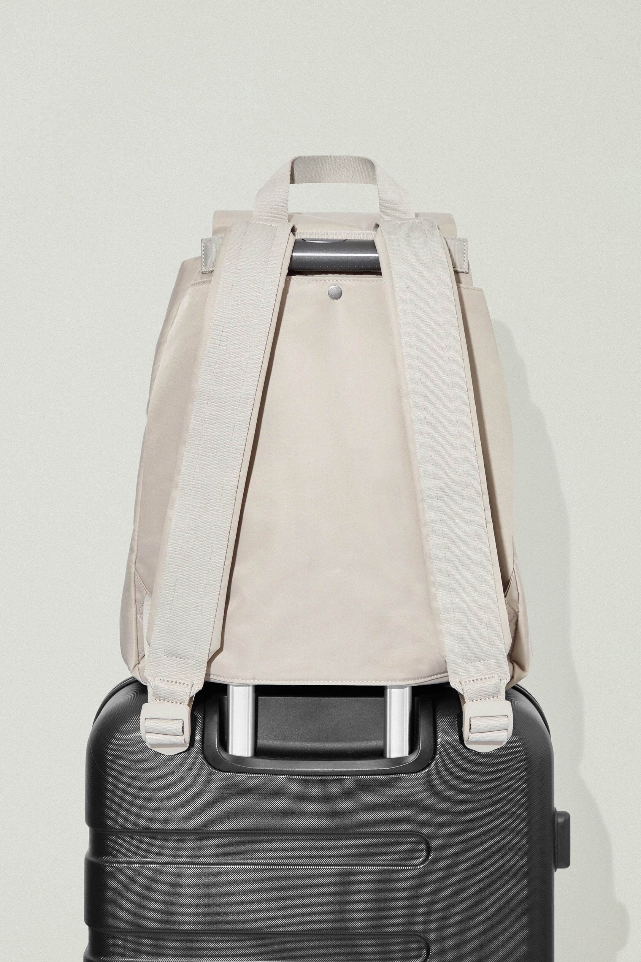 Beige backpack sitting on top of black suitcase