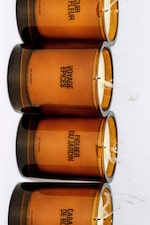 Placeholder for: Four amber-colored candle jars with white wicks on a white surface, labeled with different fragrance names.